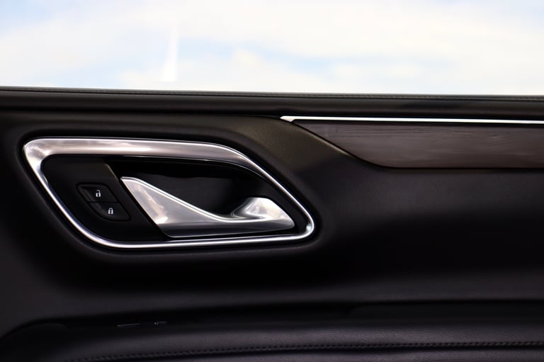Close-up of a car door handle with chrome trim and dark interior panel against a light sky background