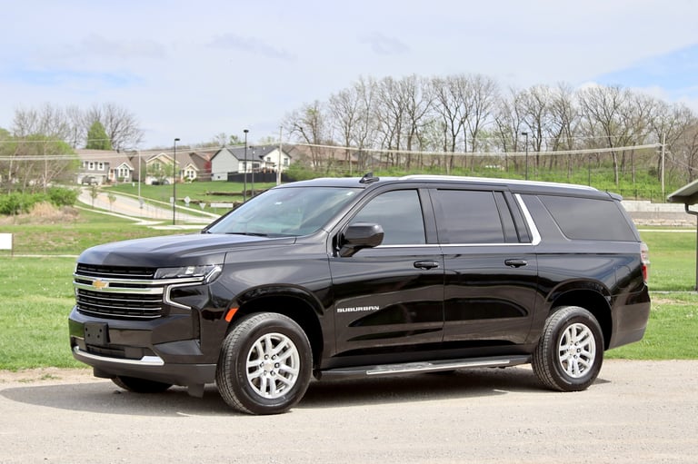 Black Chevrolet Suburban SUV parked on a driveway with rural houses and bare trees in the background