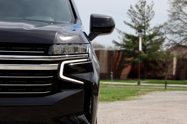 Front view of a black SUV showing headlight and grille design, parked in residential driveway with trees in background
