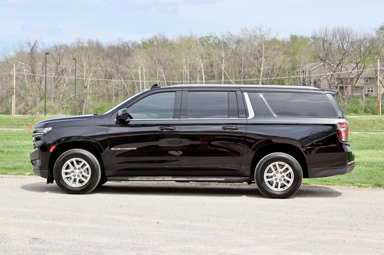 Black Chevrolet Suburban SUV parked on asphalt with bare trees and green grass in the background