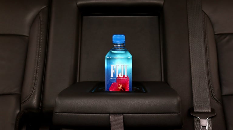 Fiji water bottle placed on a cars center console armrest between two black leather seats